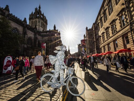 The Edinburgh Festival and Edinburgh fringe festival. A street performer drawing a crowd in a summer performance. A living statue, man in silver on a bicycle in costume. Lothian, Scotland